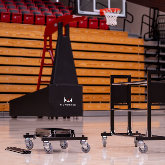 In front of a basketball hoop, one Monorack collapsed with its ball support bars removed. A second Monorack is full assembled.