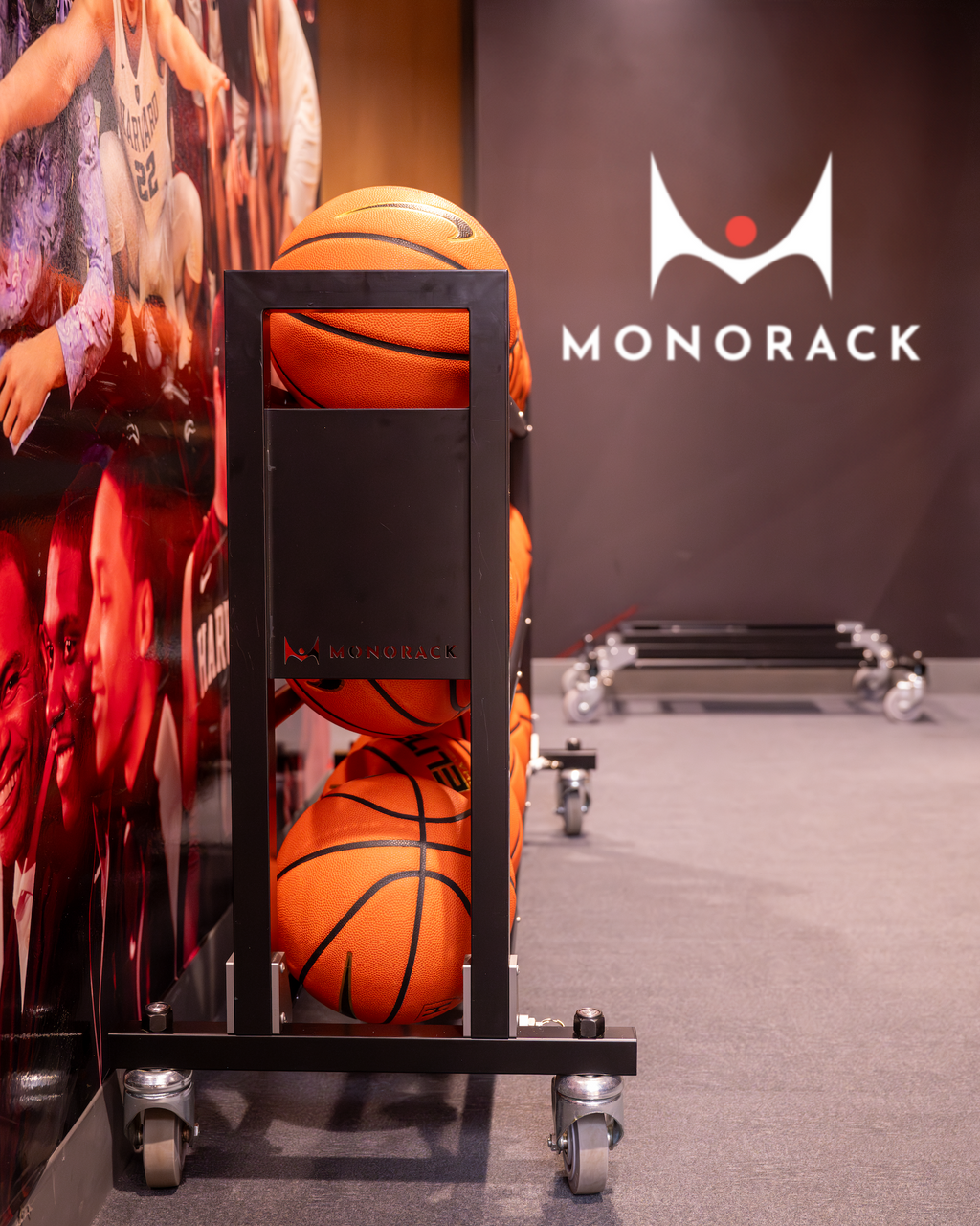 One Monorack with 15 basketballs positioned in a locker room next to a collapsed Monorack stored behind it. A Monorack logo is on the wall.